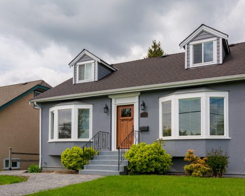Family house with green lawn and decorative bushes in front. Average residential house on cloudy day in British Columbia